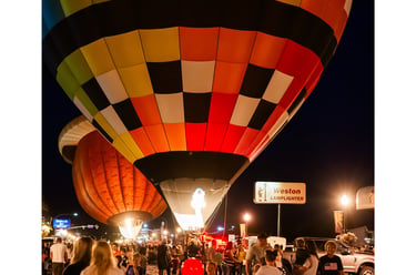 Colorful checkered hot air balloons glowing at night during a crowded summer festival event.