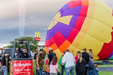 A colorful hot air balloon being inflated with a gas burner flame at an outdoor festival.