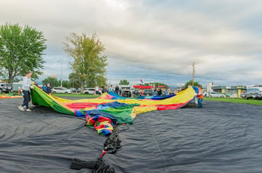 People preparing a colorful hot air balloon envelope for inflation in an outdoor grassy field.