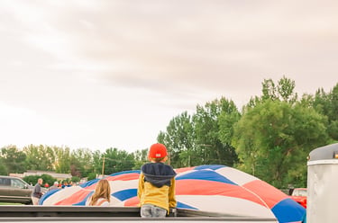 A child in a pickup truck watching a colorful hot air balloon inflate at a festival.
