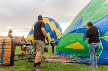 Ground crew members preparing a colorful green and blue hot air balloon for launch on a grassy field.