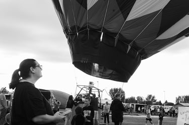 Black and white image of woman watching large hot air balloon is inflated and prepared for flight at an outdoor festival.
