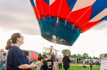 A colorful red, white, and blue hot air balloon being prepared for flight at an outdoor festival.