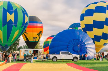 Colorful hot air balloons inflating at an outdoor festival with spectators and a white pickup truck.