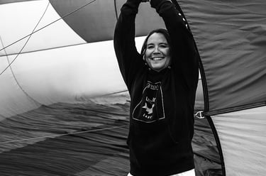 A smiling woman in a black hoodie holding open a large hot air balloon envelope during setup.