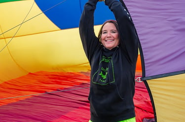A woman holds open a colorful rainbow hot air balloon envelope during inflation.