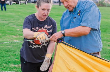 A man and woman prepare a yellow hot air balloon envelope for flight in a grassy field.