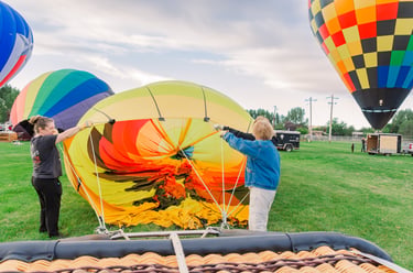 Ground crew inflating a colorful hot air balloon envelope on a grassy field during a festival.