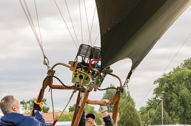 Ground crew preparing a hot air balloon basket and burner for flight at an outdoor festival.