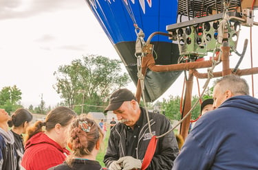 A hot air balloon pilot demonstrates burner equipment to a group of people at a balloon festival.