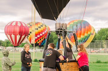 A group of people prepares a hot air balloon for flight in a grassy field during a colorful balloon festival.