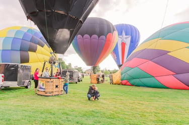 Colorful hot air balloons preparing for takeoff on a green grass field during a festival.