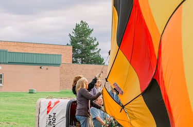 A ground crew prepares a colorful hot air balloon for inflation on a grassy field.