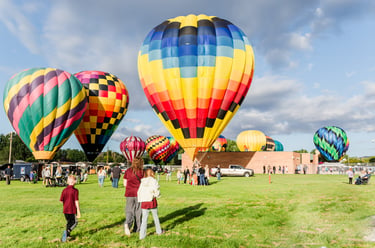 Colorful hot air balloons taking off from a green field at a summer festival with spectators.