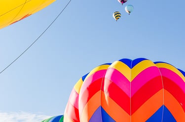 Colorful hot air balloons with chevron patterns floating in a clear blue sky during a festival.