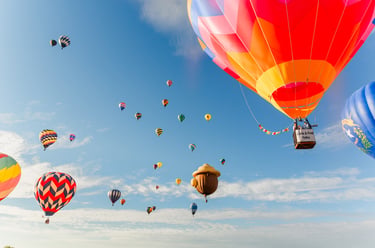 Colorful hot air balloons and a unique acorn balloon floating in a clear blue sky during a festival.