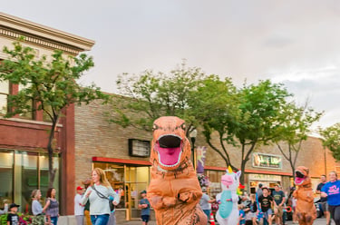 A group of people running down a city street in inflatable T-Rex dinosaur costumes during a fun run event.