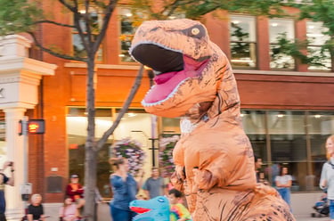 A person wearing a funny inflatable T-Rex dinosaur costume running down a city street during a parade.