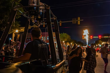 Hot air balloon burner glowing at a night festival with crowds on a city street.