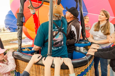 Excited family and crew preparing a colorful hot air balloon for flight with a wicker basket.