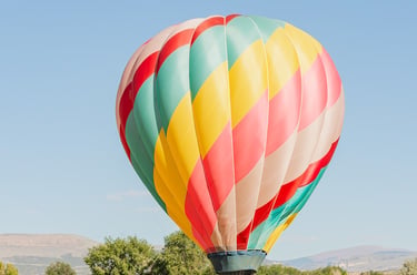 Colorful hot air balloon taking off from a golden field with mountains in the background.