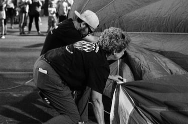 A black and white photo of people preparing a hot air balloon for inflation at an outdoor festival.
