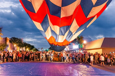 A colorful hot air balloon inflating over a crowded city street during a festive evening event.