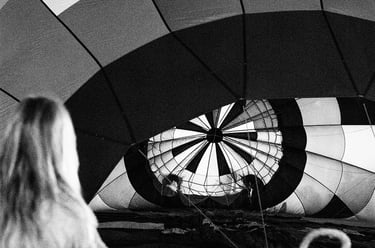 Black and white photo of a person watching a checkered hot air balloon being inflated.