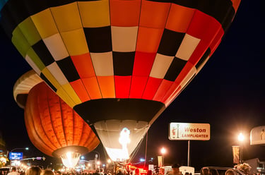 Crowd watching colorful hot air balloons glowing at night during a festival glow event.