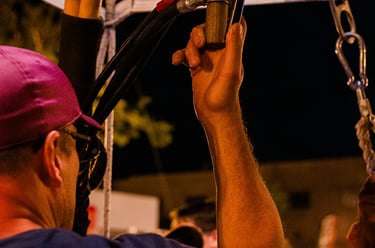 A hot air balloon pilot operates the propane burner system during a night glow event.