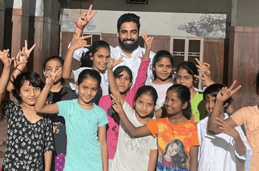 Vikash Sharma with a group of cheerful young girls making peace signs at a school or community center