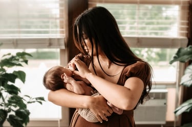 Mother cradling newborn son by a window at home in Hibbing, MN