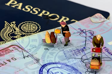 Miniature figurine pushing luggage cart on a stamped passport, illustrating visa application process
