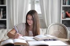 Young woman doing research at a desk with several books open.