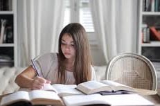 Young woman doing research at a desk with several books open.