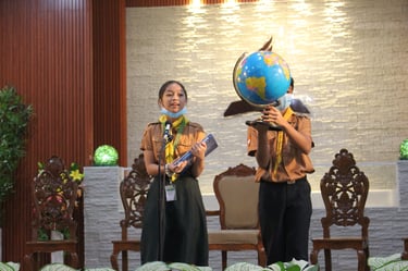2 elementary scout students with a book and globe speaking on a stage