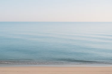 wide shot of a calm sea with empty shoreline, evoking longing and absence.