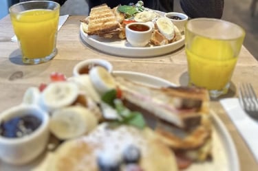 Assiettes de brunch avec pancakes, fruits, gaufres, confitures et verres de jus d’orange.