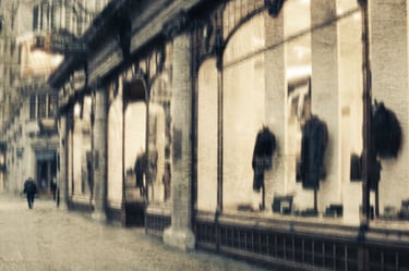 Softly blurred London street scene with a pedestrian walking past illuminated shop windows displaying coats and reflections