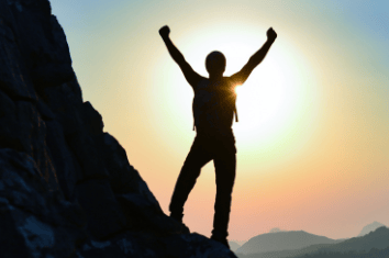 a person standing on a rock formation with a sun setting in the background
