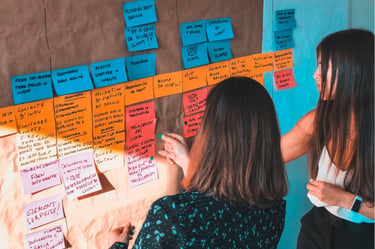 Two people brainstorming and writing on colorful sticky notes and a whiteboard, showcasing collaborative business strategy