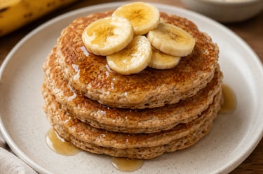 Stack of fluffy whole wheat banana pancakes topped with fresh fruit slices and maple syrup on a plate.