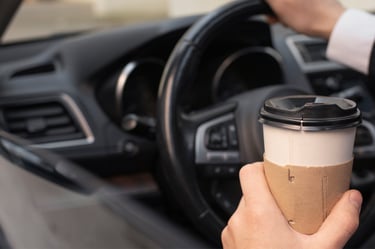 Client serein assis dans sa nouvelle voiture, tenant un café à la main.