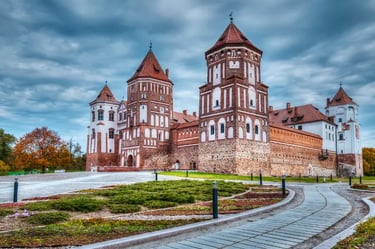 The historic Mir Castle Complex in Belarus featuring red brick Gothic architecture under a dramatic cloudy sky.