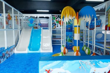 Indoor soft play area with blue slides, ball pit, and ocean-themed decorations for kids' entertainment.