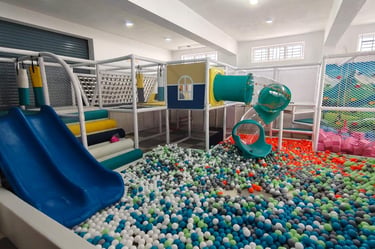 Indoor playground for kids featuring a large ball pit, blue slides, and a white climbing structure with tubes.