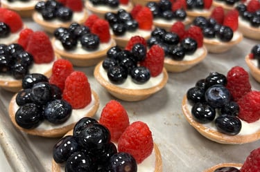 Mini fruit tarts with vanilla cream, fresh blueberries, and raspberries on a baking sheet.