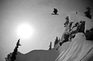 a black and white photo of a snowy slope and a man on skis in the air