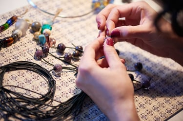 Manos creando una joya artesanal en macramé, ensamblando cuentas de colores con cuidado y precisión sobre un mesa