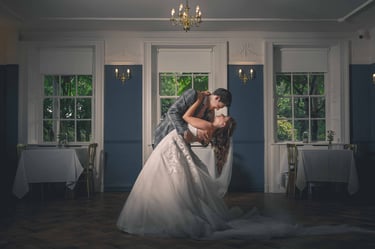 A groom dips his bride during their first dance in an elegant wedding ballroom with blue walls.
